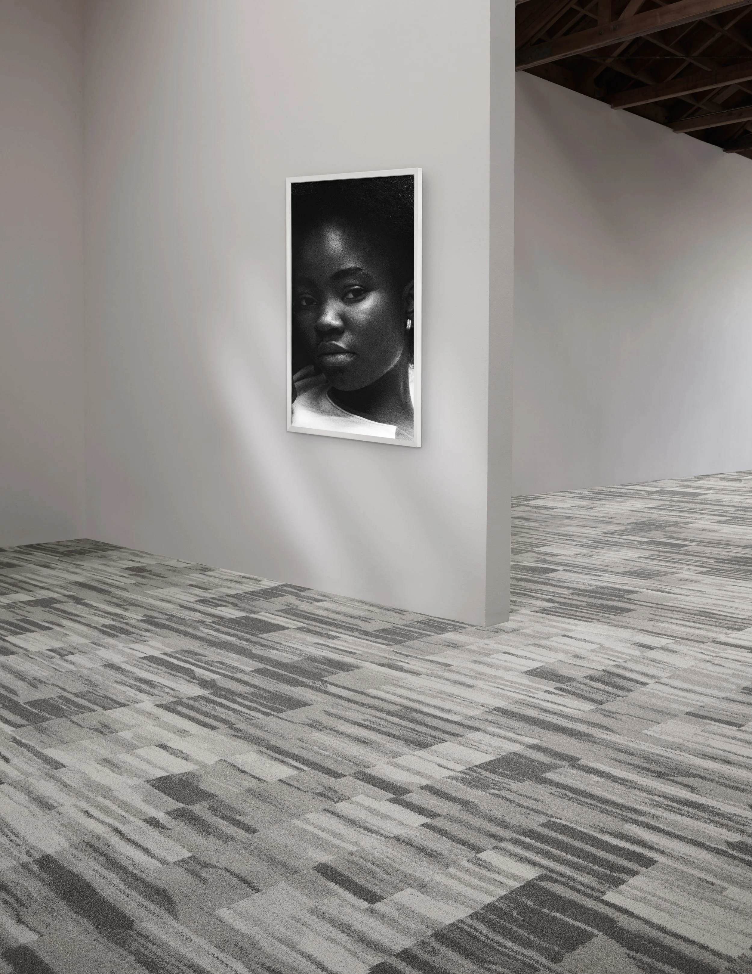 Gallery wall with a black-and-white portrait above patterned gray carpet and wooden ceiling trusses.