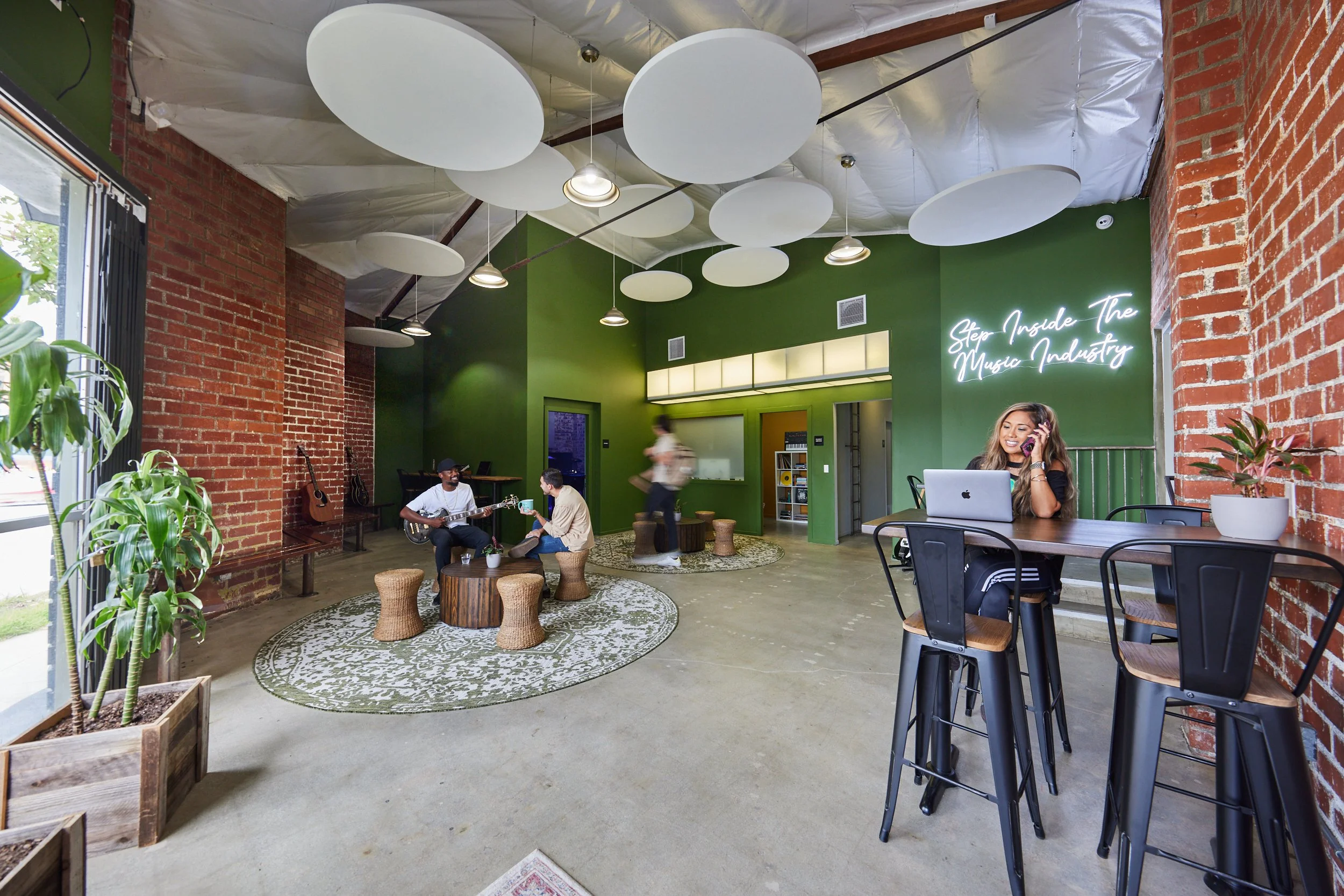 Creative studio lounge with olive-green wall, brick, circular acoustic clouds, and people at work.