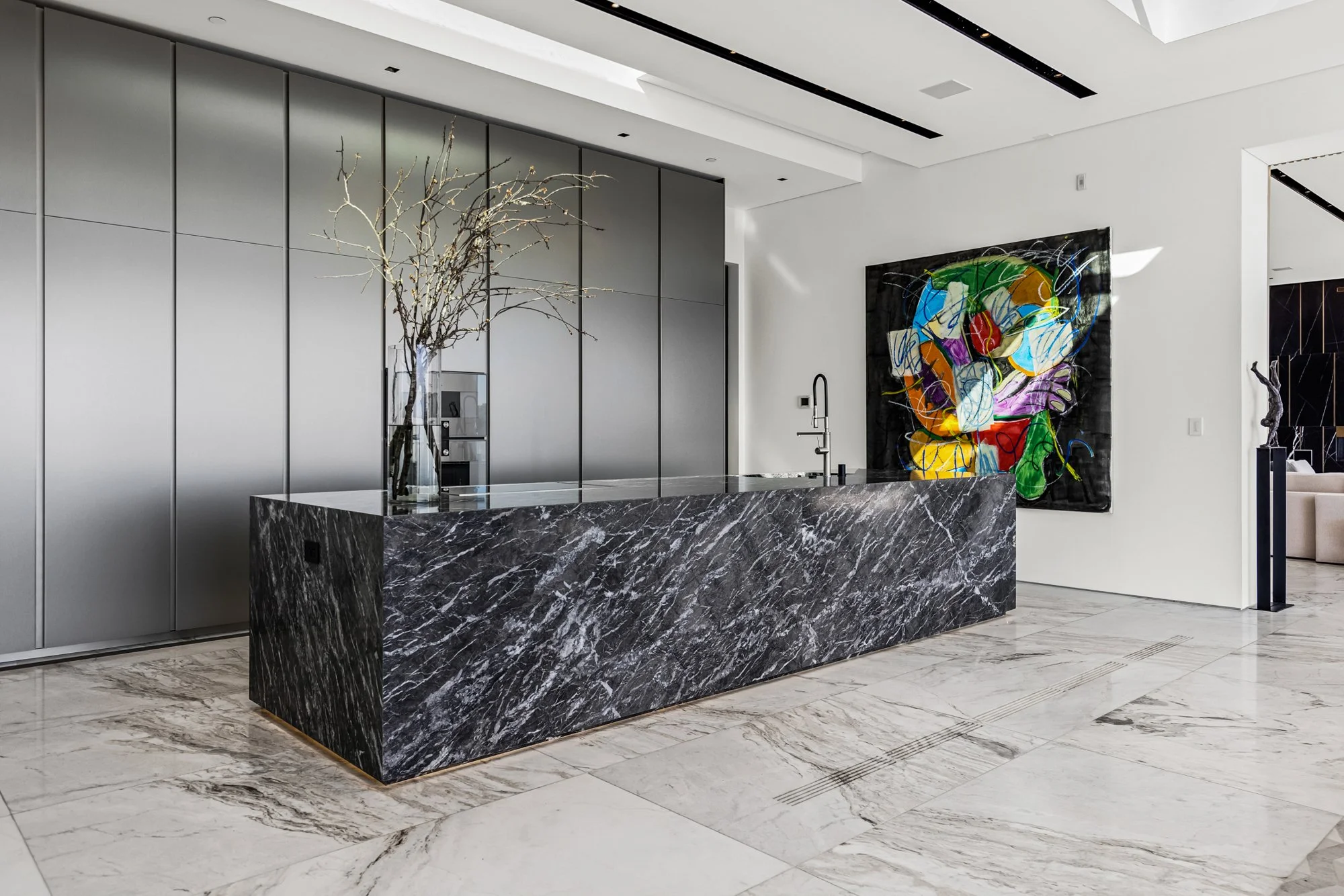 Kitchen with a dark marble island, pale stone floors, and floor-to-ceiling silver cabinetry.