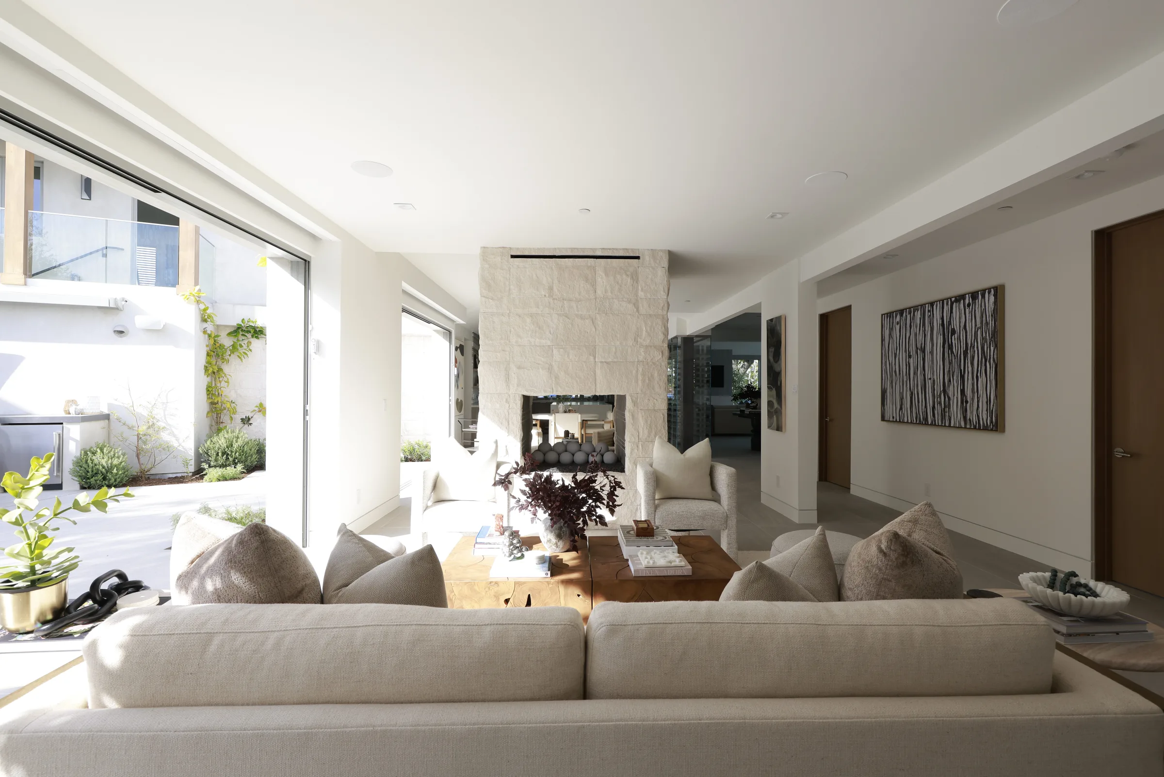 Living room with a stone fireplace and cream seating opening to a patio and outdoor kitchen.
